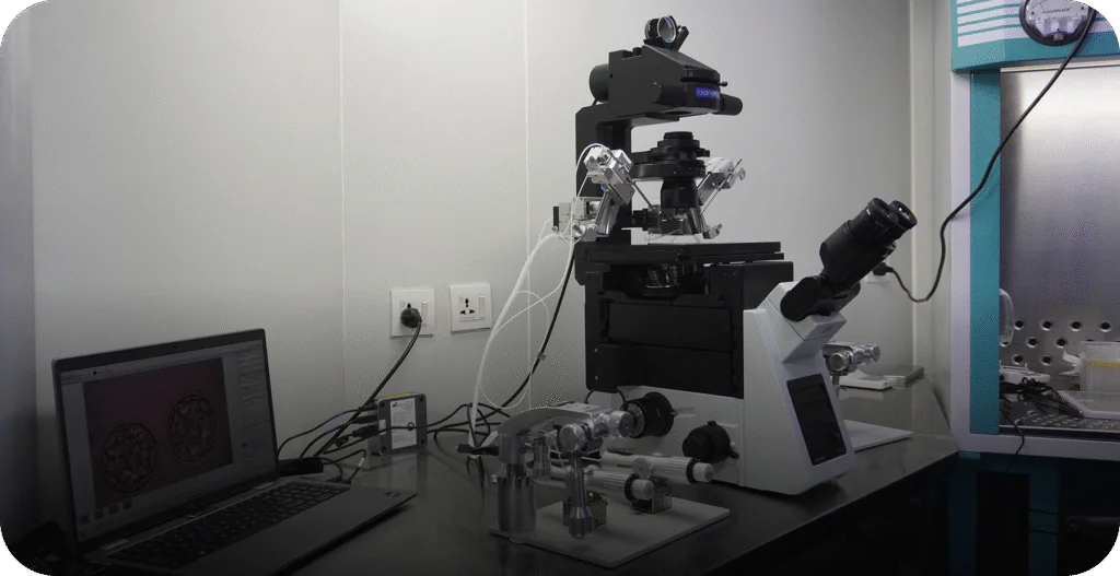 IVF workstation with an inverted micromanipulation microscope and a laptop displaying high-quality embryos. - AAS Fertility